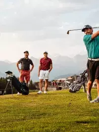 Un trou d'eau sur le parcours de golf des Arcs, reflétant les montagnes alpines et le ciel bleu, avec un golfeur sur le green à l'arrière-plan, en été.