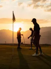 Joueurs de golf sur un green au coucher du soleil en montagne.