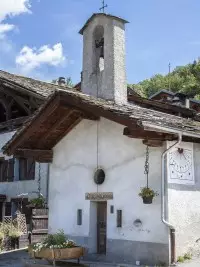 Ancienne chapelle en pierre avec clocher et cadran solaire dans un village de montagne.