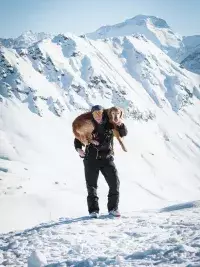 Pisteuse portant un chien de secours dans un décor alpin enneigé.