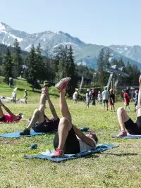 Une participante effectue un exercice de renforcement musculaire avec un élastique lors d'une séance de fitness en plein air aux Arcs, encadrée par un coach