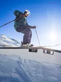 Gros plan d'un skieur en équilibre sur un rail de fer au snowpark des Arcs, illustrant la zone de jib et les modules techniques du parc