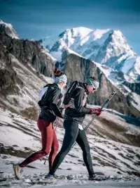 Un trailer court sur un sentier en balcon offrant une vue imprenable sur le Mont-Blanc enneigé, avec la station des Arcs et les montagnes de la Tarentaise en arrière-plan